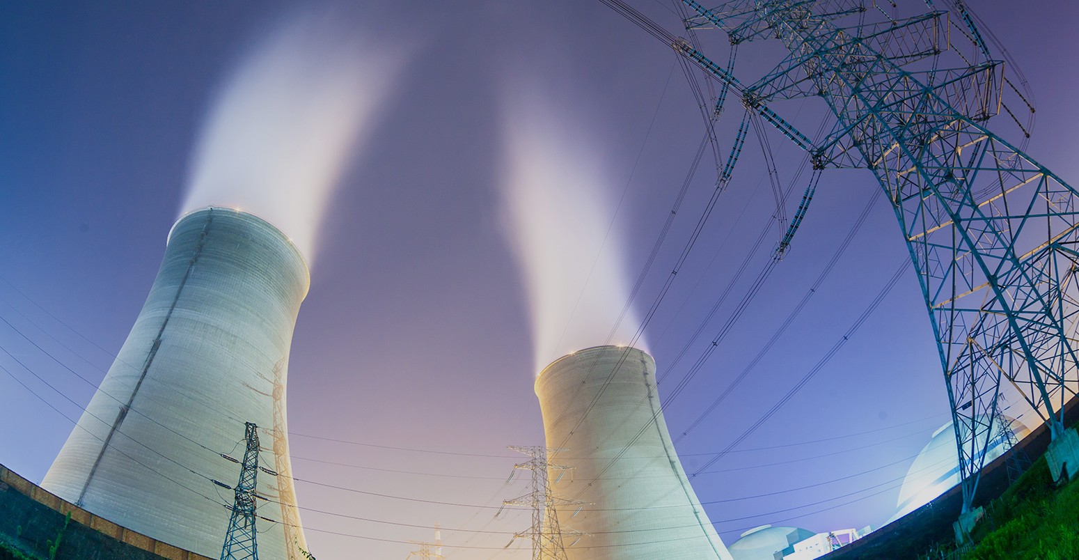 Upward view of the cooling towers and high voltage power transmission tower at night.