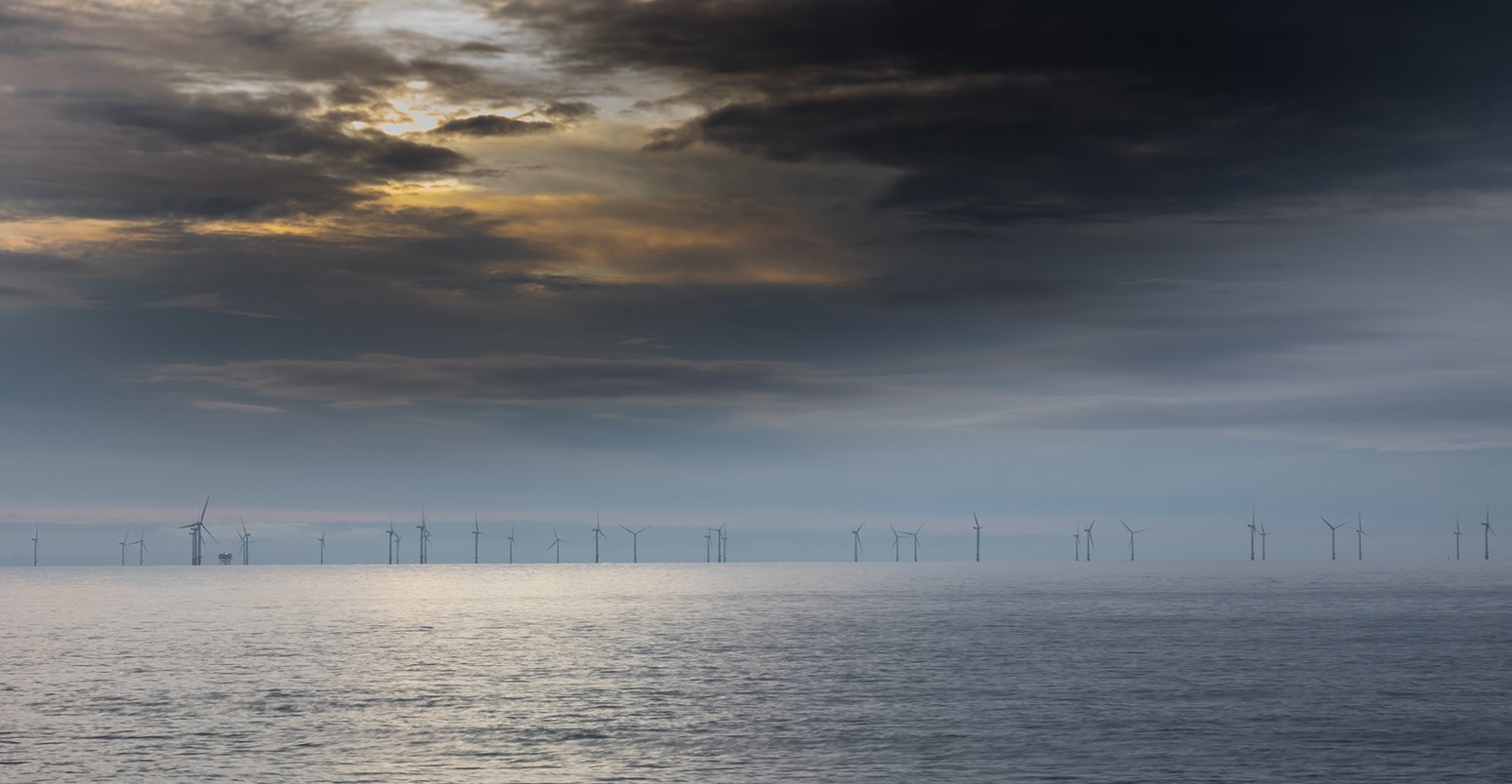 distant off shore wind turbine farm set against a background of storm clouds at sunrise