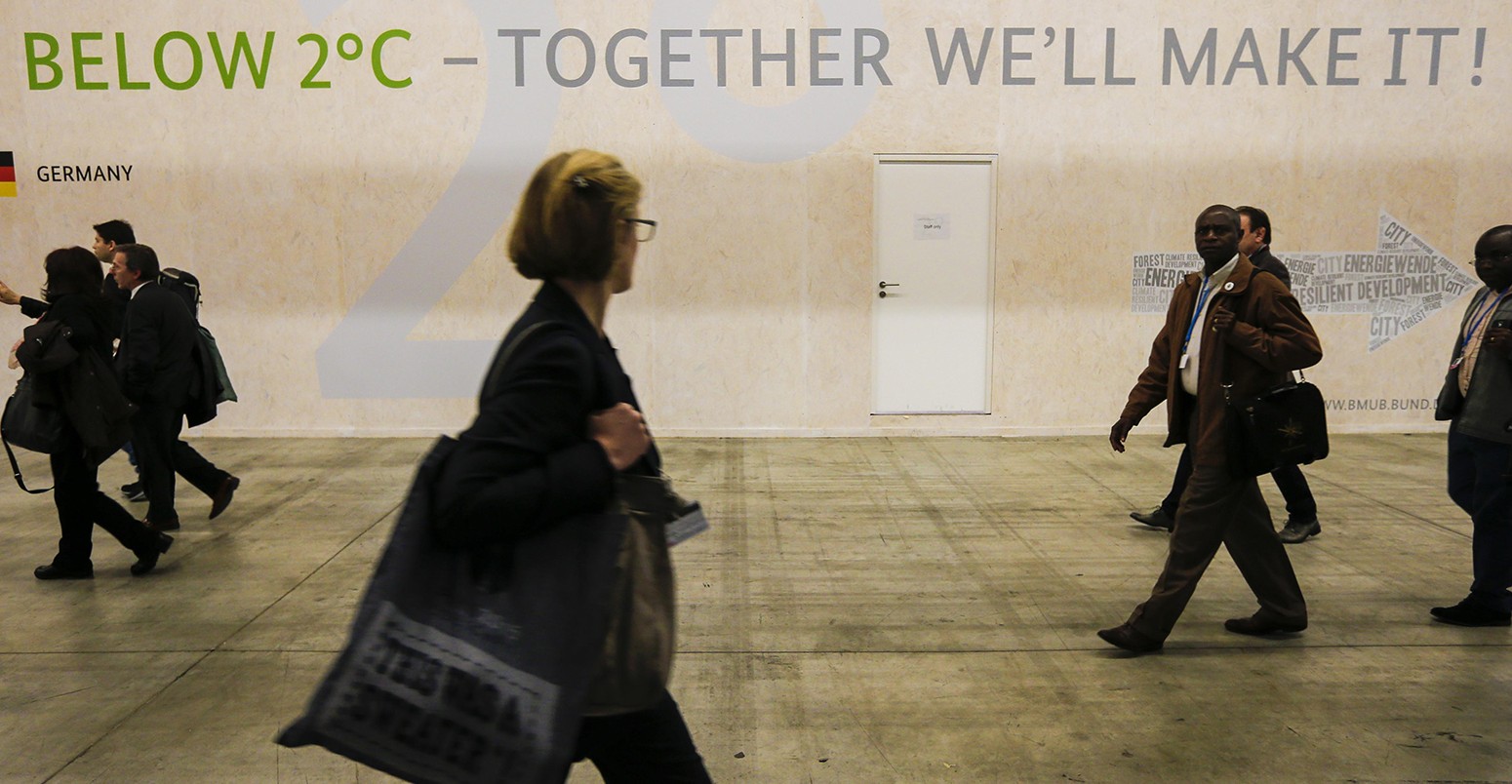 People walk past the slogan of 'Below 2 degrees' at the site of the 2015 United Nations Climate Change Conference (COP 21) at Le Bourget on the northern suburbs of Paris, France, Dec. 2, 2015.