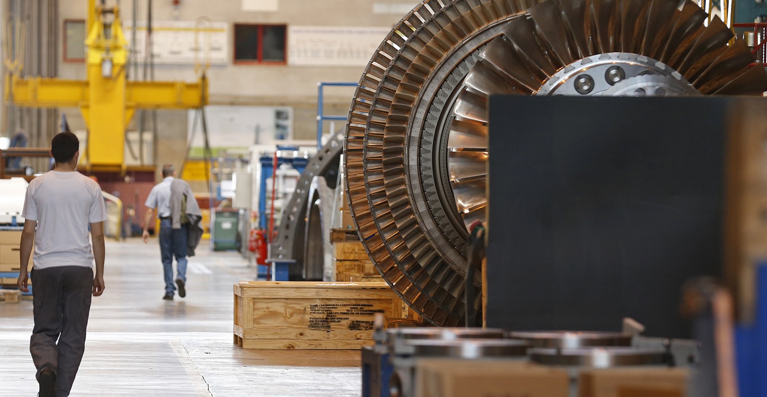 A worker walks past a gas turbine under construction at the gas turbines production unit of the General Electric plant in Belfort