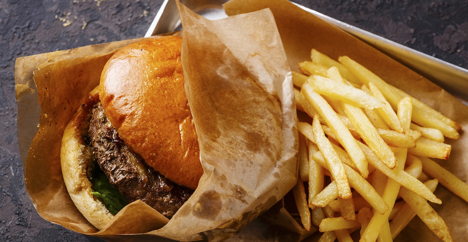 Burger with meat and French fries in aluminum tray on dark background