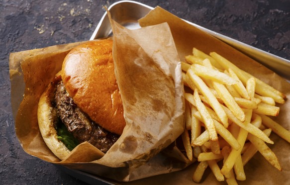 Burger with meat and French fries in aluminum tray on dark background