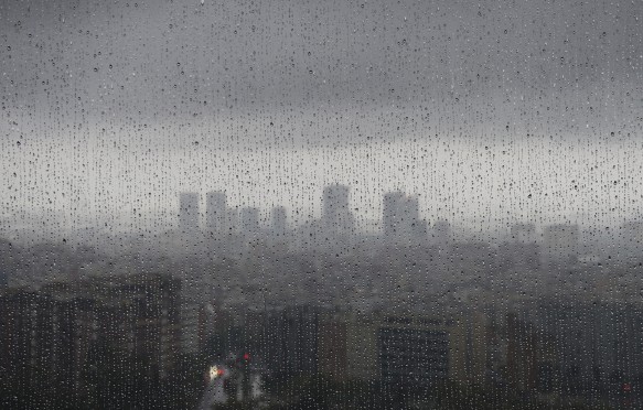 After heavy rainfall, the diffuse skyline of Barcelona is emerging in the twilight behind raindrops on a window
