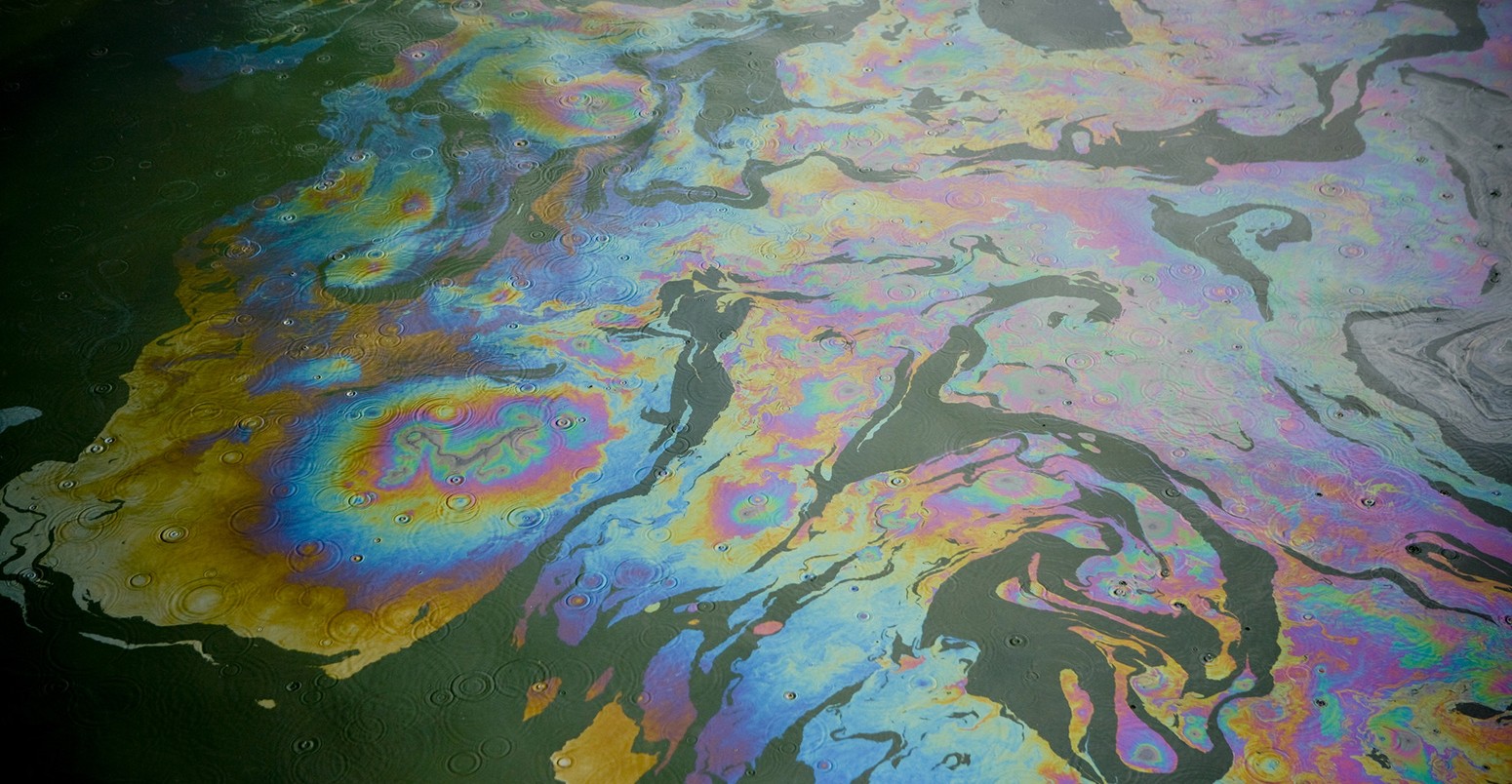 Diesel oil spill on the water surface during a light rain storm.