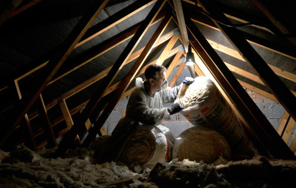 BCMCX8 MAN INSULATING A DOMESTIC HOUSEHOLD LOFT WITH ROLLS OF LOFT INSULATION UK