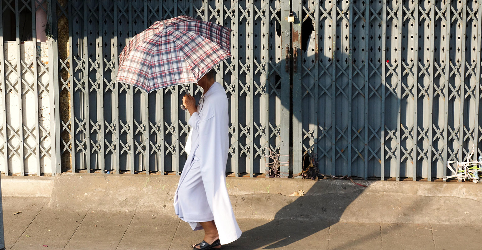 EE03A2 Buddhist Man with umbrella against sun walking in street, Bangkok, Thailand, Southeast Asia.
