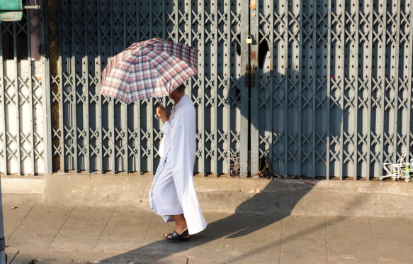 EE03A2 Buddhist Man with umbrella against sun walking in street, Bangkok, Thailand, Southeast Asia.