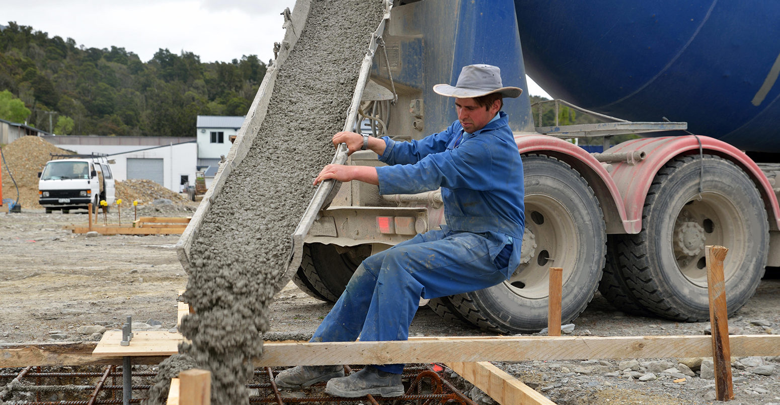 EFA7E6 A builder directs wet concrete from a cement truck into the foundations of a large building.