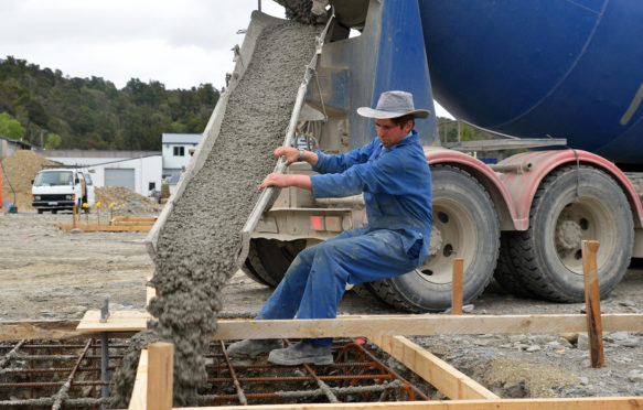 EFA7E6 A builder directs wet concrete from a cement truck into the foundations of a large building.