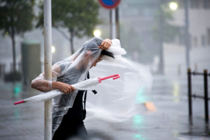 A woman clings on as typhoon Roke blows through Tokyo, Japan, 21 September 2011. Credit: Robert Gilhooly / Alamy Stock Photo. C7G6KM