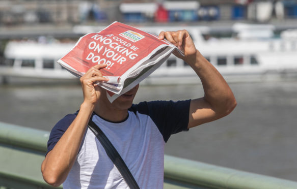 A pedestrian on Waterloo Bridge shelters with a newspaper from the sun. 25 July 2019, London.