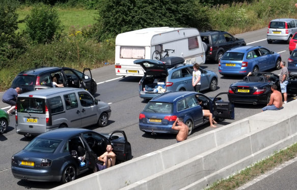 People stuck in a traffic jam in Somerset, UK, leave their cars during a heatwave on 30 July 2016. Credit: Timothy Large / Alamy Stock Photo. GFAT52
