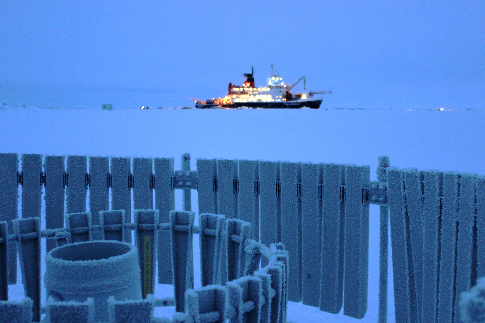 Foreground: A “precipitation bucket”  – used to collect snowfall – surrounded by a windshield at MOSAiC’s “Met City”. Background: The Polarstern. 