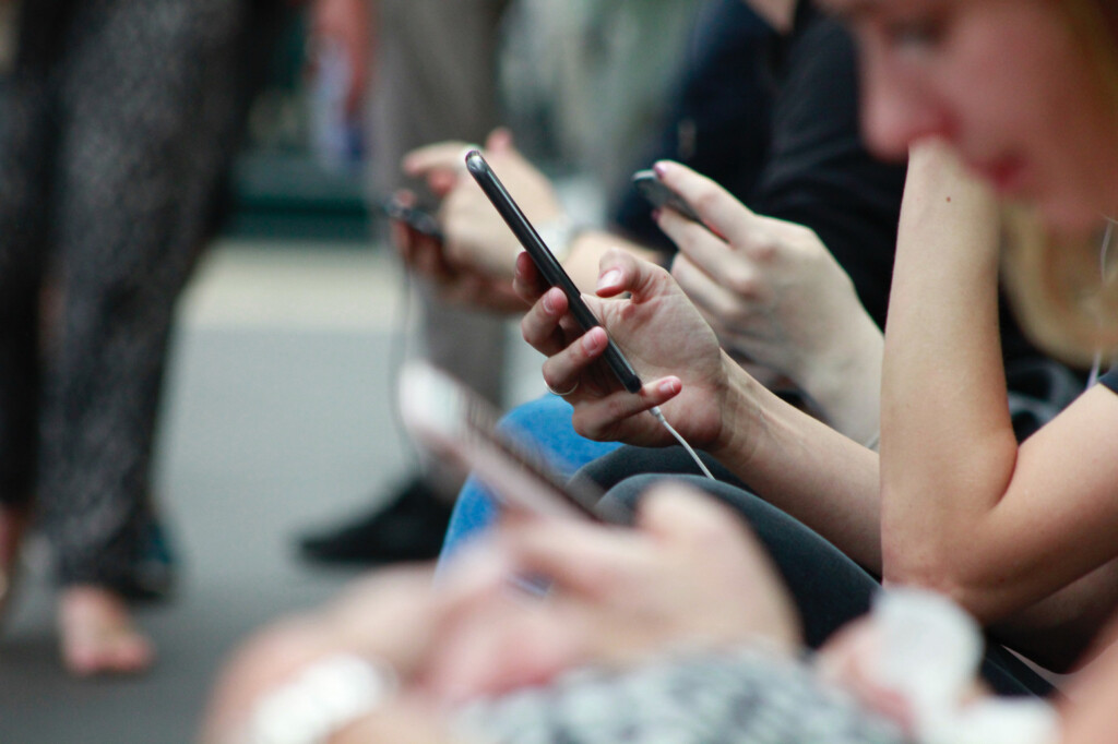 Smart phone users wait at a train station.