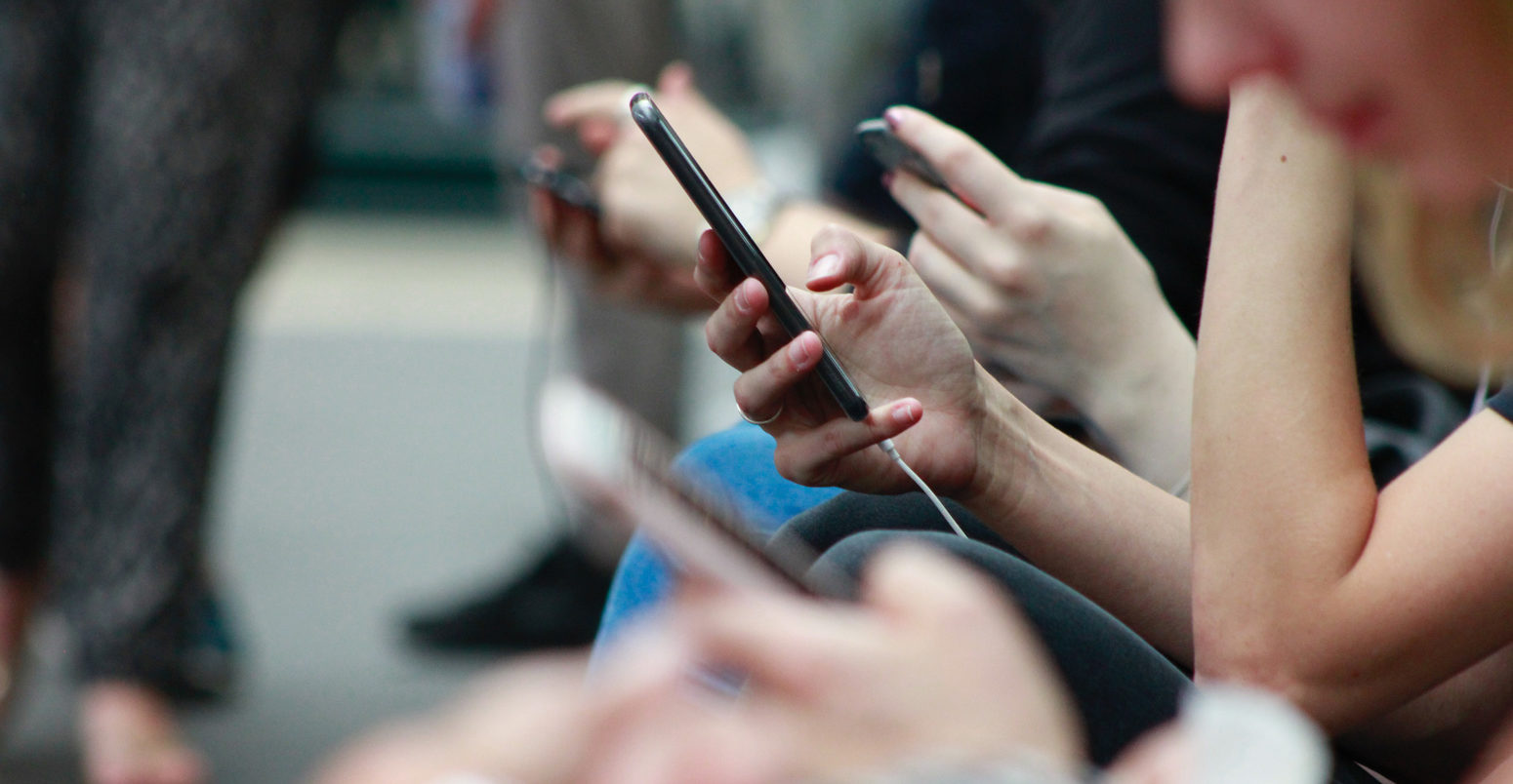 Smart phone users wait at a train station.