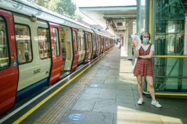 A passenger wearing a facemask standing on the London Underground platform using a fan to cool down from the heat and humid conditions during the August heatwave.