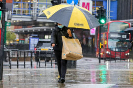 A-shopper-wearing-a-face-mask-shelters-from-the-rain-underneath-an-umbrella-on-a-wet-and-windy-day-caused-by-Storm-Alex