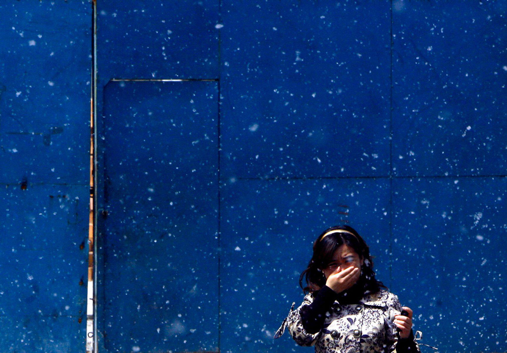 A woman tries to cover her mouth as she walks through cotton-like seeds from Poplar trees on a spring day in Beijing