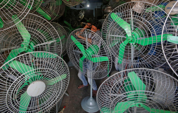 A mechanic uses a hammer to fix steel guard of an electric fan inside a shop in Mumbai
