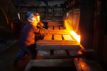 A hot steel billet is removed from furnace as a cold billet waits in foreground