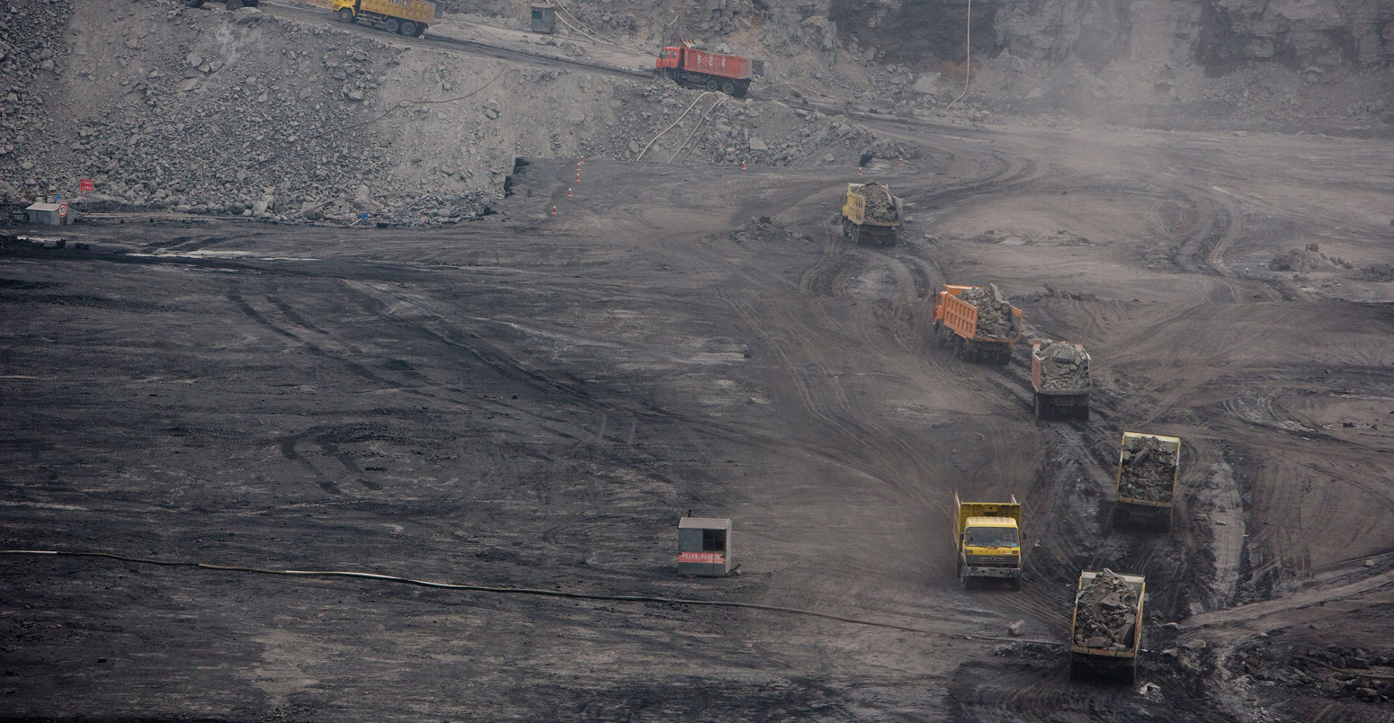 A procession of 50 ton trucks are loaded with overburden on their way to a spoil heap at a new open cast mine near Ordos, China