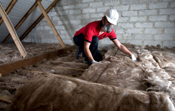 A worker lays loft insulation in the attic of a residential property in Cornwall, UK