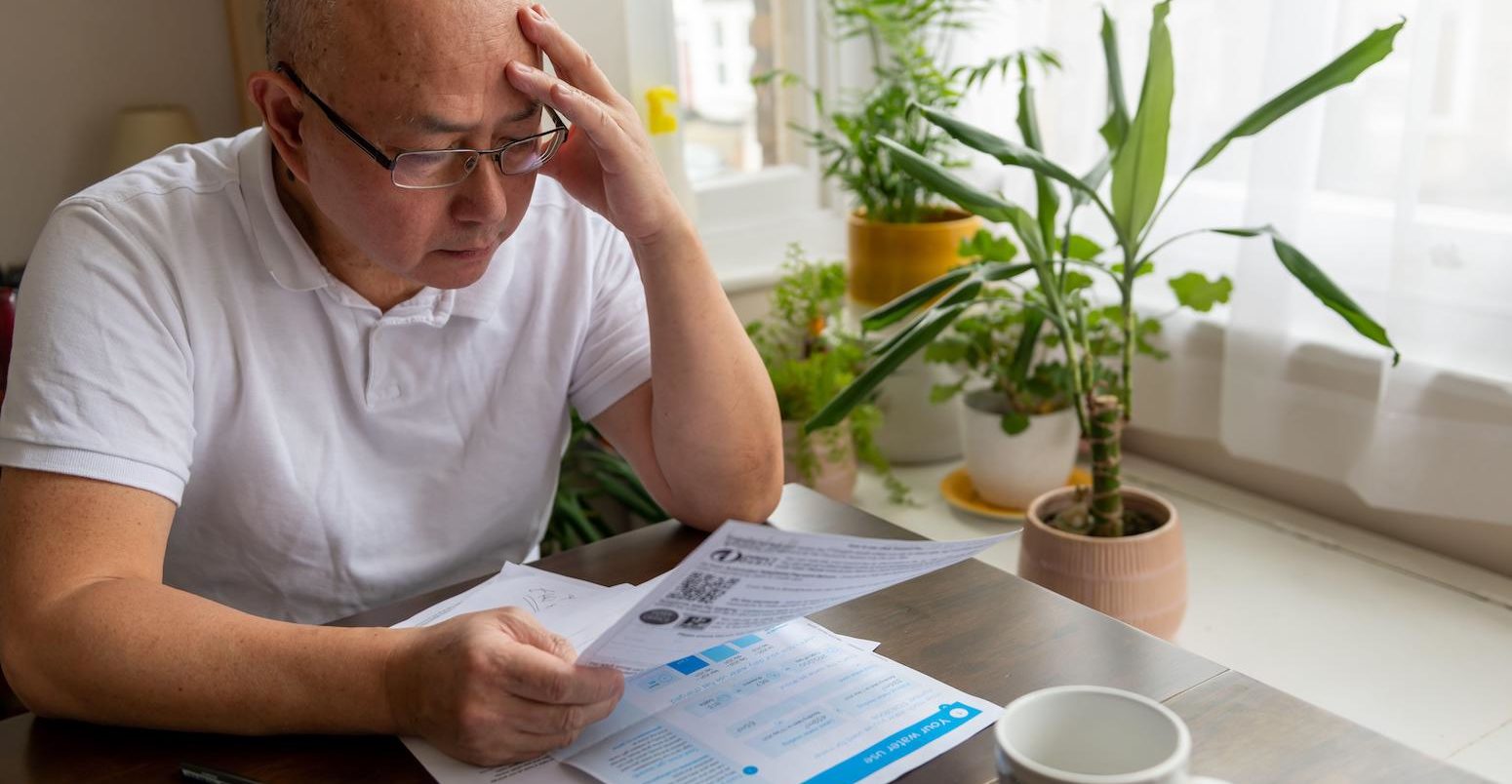 A senior man holding his head trying to cope the raising cost of energy and tax bills