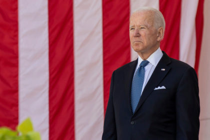 US President Joe Biden stands in front of the United States national flag