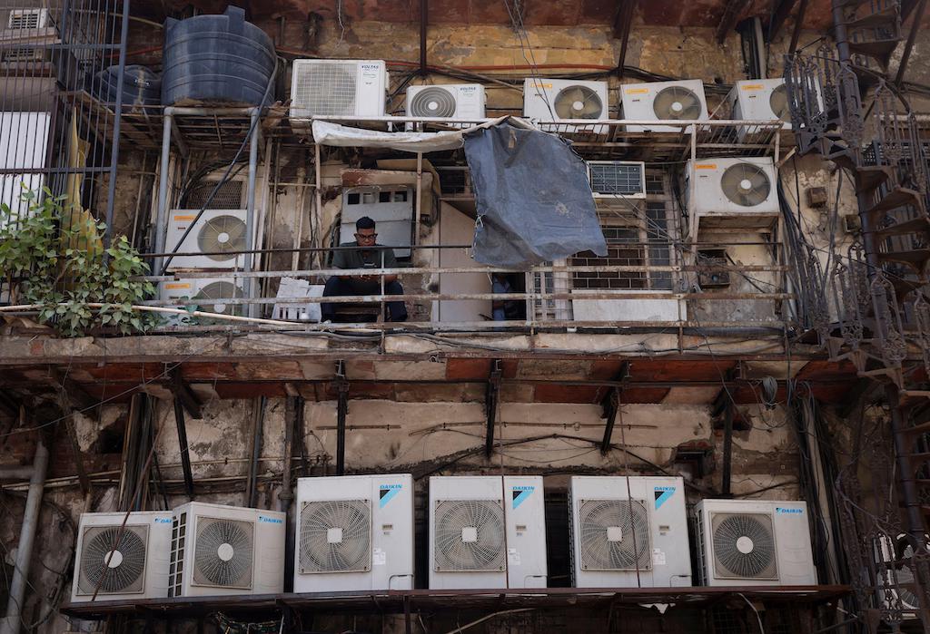 A man uses his mobile phone as he sits amidst the outer units of air conditioners, at the rear of a commercial building in New Delhi, India on April 30, 2022.