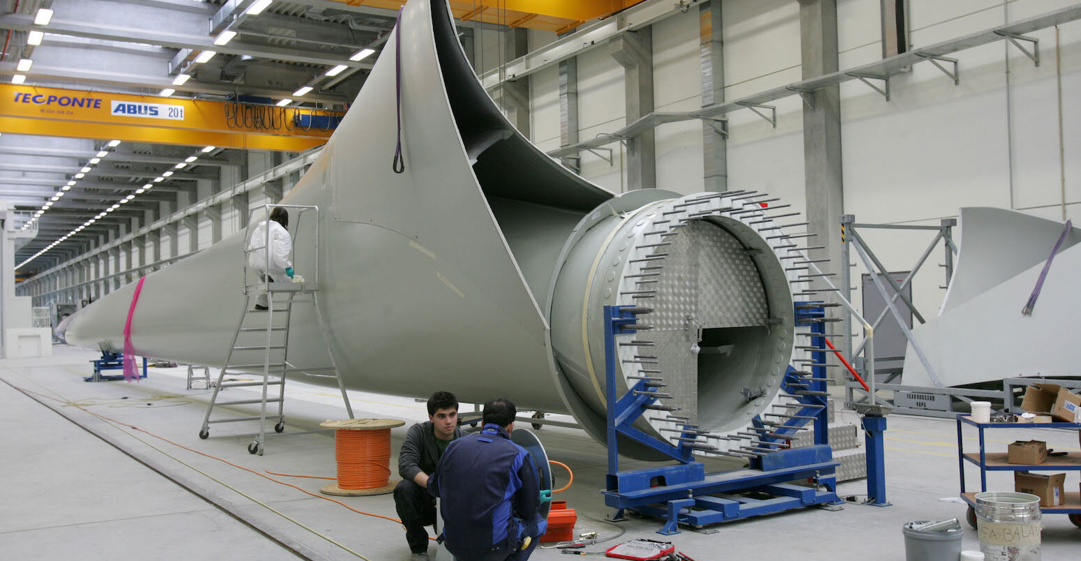 Workers next to a giant wind turbine blade at the factory VentoMoinho at Viana do Castelo, Portugal.