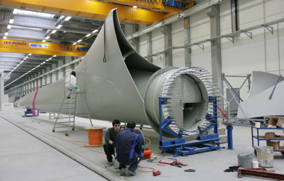 Workers next to a giant wind turbine blade at the factory VentoMoinho at Viana do Castelo, Portugal.