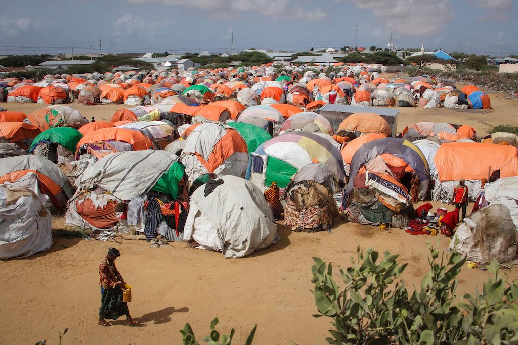Somalis who fled drought-stricken areas walk next to a cluster of makeshift shelters at a camp for the displaced on the outskirts of Mogadishu, Somalia, on 4 June 2022.