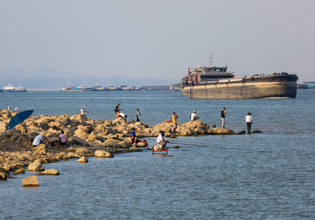 | People fish on a hot day as a cargo ship travels along China | MR Online's largest freshwater lake, Poyang Lake, in Jiangxi, on 28 August 2022.