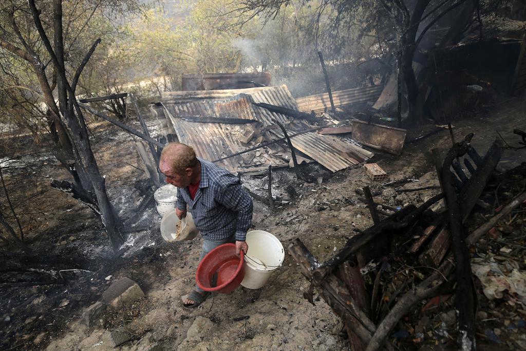 A man walks past a house burned down in a wildfire Algeria.