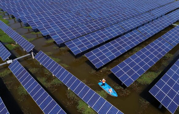 Workers boat past solar panels in a floating solar energy farm in Jingzhou, China. Image ID: W791EX.