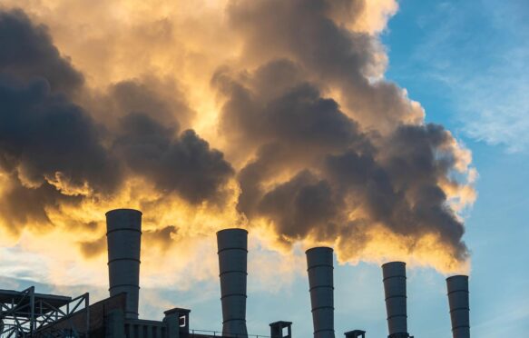 Industrial chimneys spewing smoke and soot in the blue sky polluting the air and contributing to climate change.