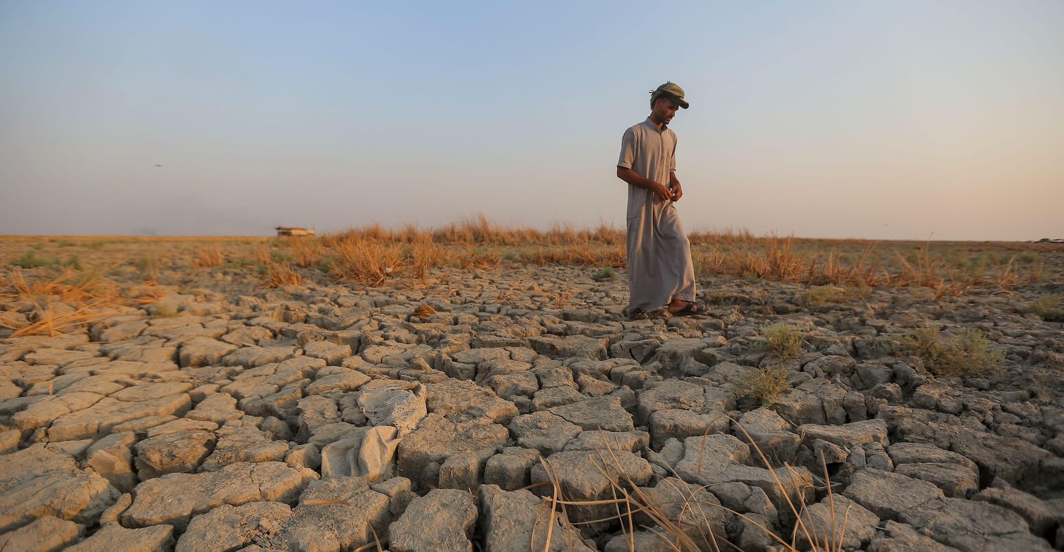 A fisherman walks across a dry patch of land after drought in the marshes of southern Iraq, Dhi Qar province. Image ID: 2M9TRTP.