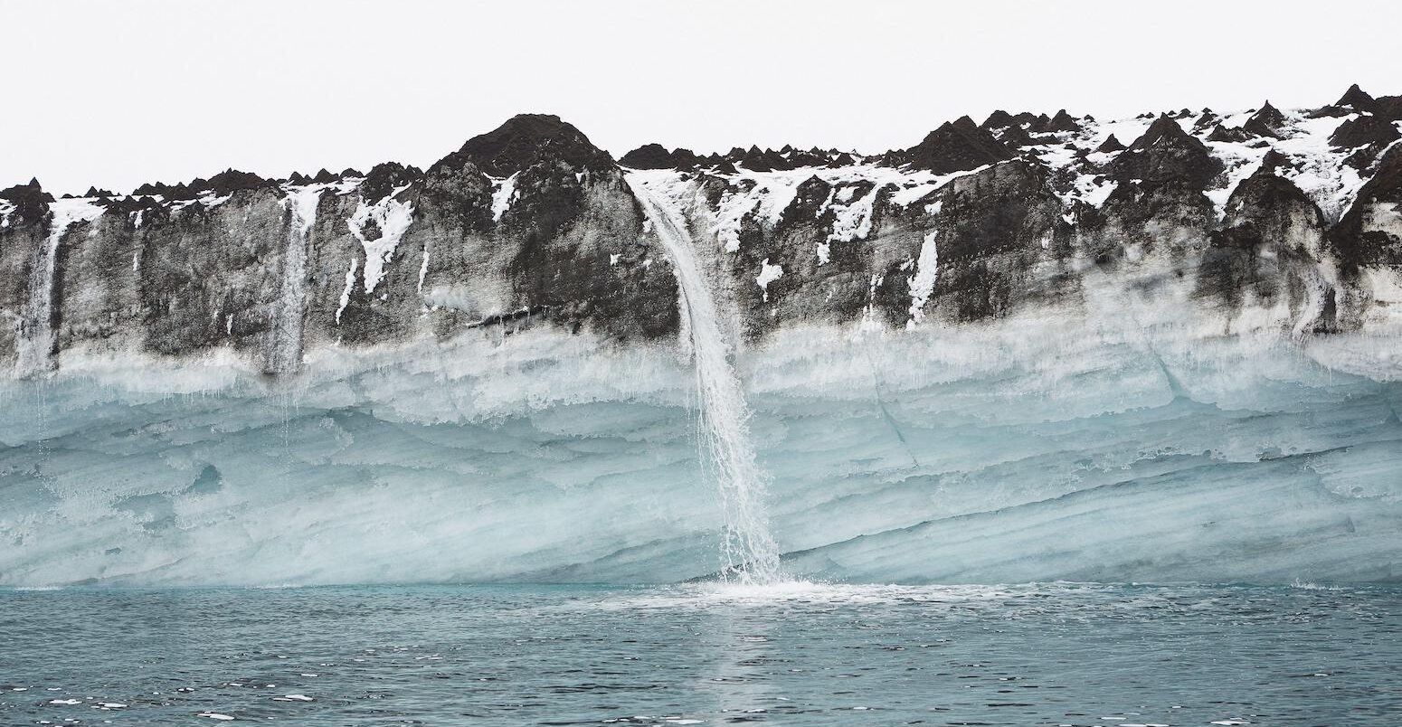 Snowmelt waterfall pouring over cliffs into ocean, Antarctic Peninsula, Weddell Sea, Antarctica.