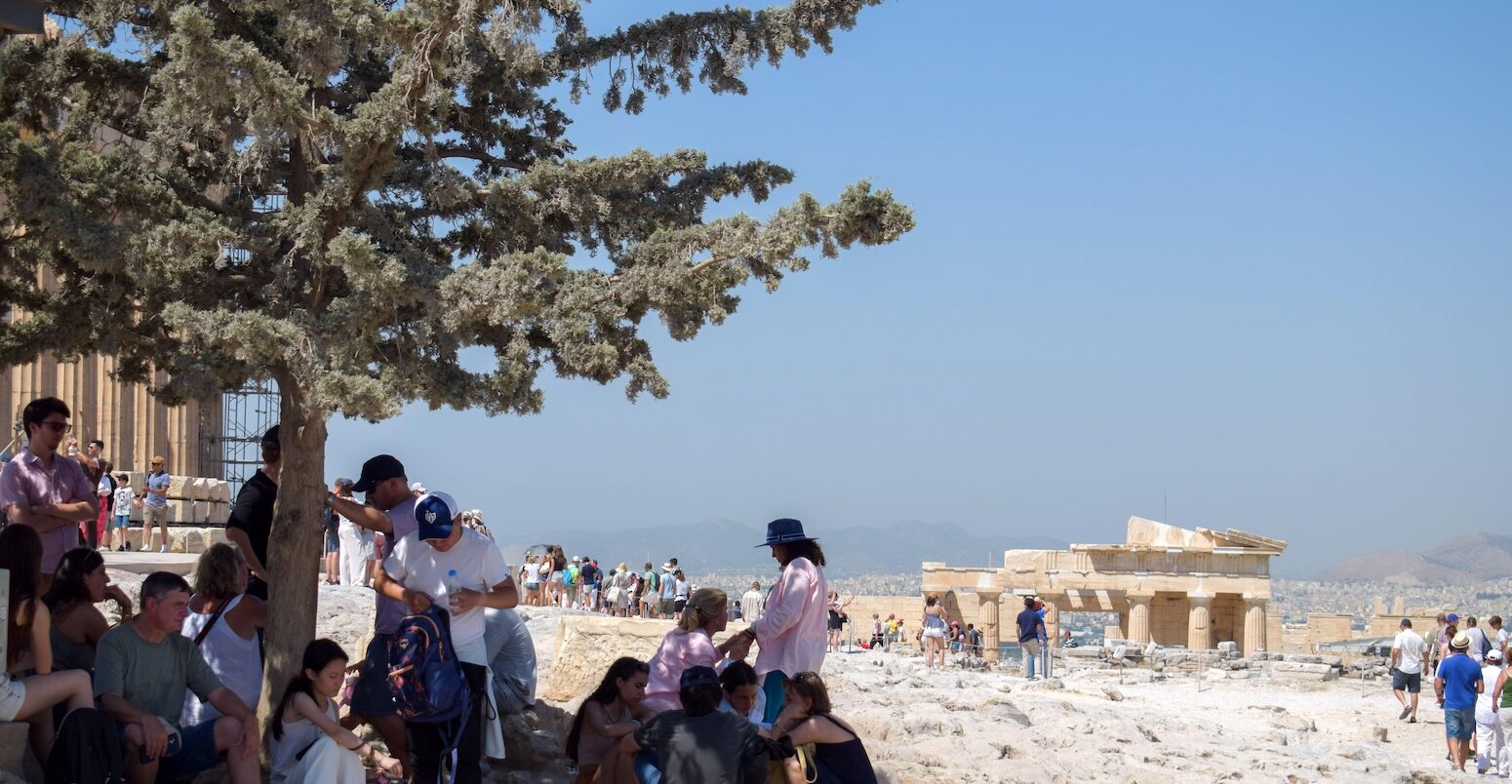 A group of tourists huddled under a tree whilst visiting the Acropolis, Athens, Greece.