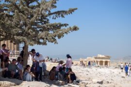 A group of tourists huddled under a tree whilst visiting the Acropolis, Athens, Greece.