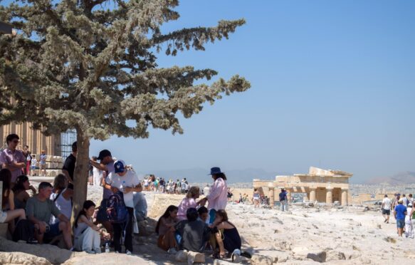 A group of tourists huddled under a tree whilst visiting the Acropolis, Athens, Greece.