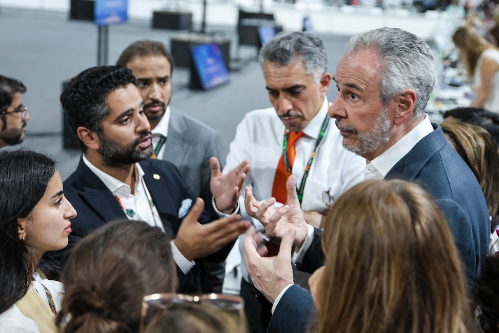 Saudi negotiators in conversation with COP30 president André Corrêa do Lago. Do Lago is on the left with his eyebrows raised, and 9 negotiators can be seen gathered around him, all people forming a circle.