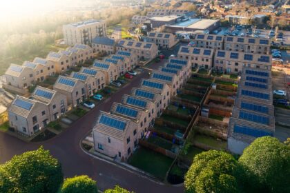 An almost birds-eye view of houses. Rows of new-build houses going from the bottom left hand corner to the middle of the image. More houses are in rows perpendicular to this, in the top right hand corner of the photo. All houses have roof-topped solar, a garden and a drive.
