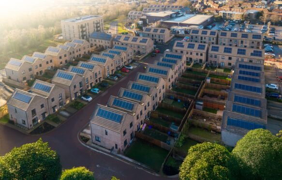 An almost birds-eye view of houses. Rows of new-build houses going from the bottom left hand corner to the middle of the image. More houses are in rows perpendicular to this, in the top right hand corner of the photo. All houses have roof-topped solar, a garden and a drive.
