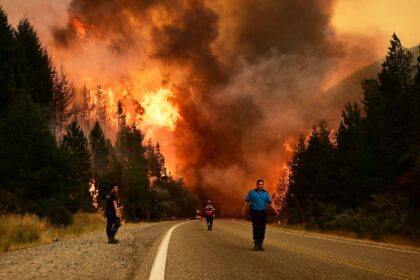 People walking on a road as a wildfire blazes behind them in Argentina, January 2026. Credit: Associated Press / Alamy Stock Photo.