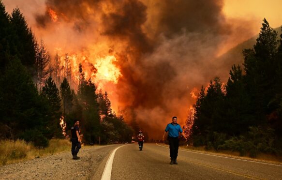 People walking on a road as a wildfire blazes behind them in Argentina, January 2026. Credit: Associated Press / Alamy Stock Photo.