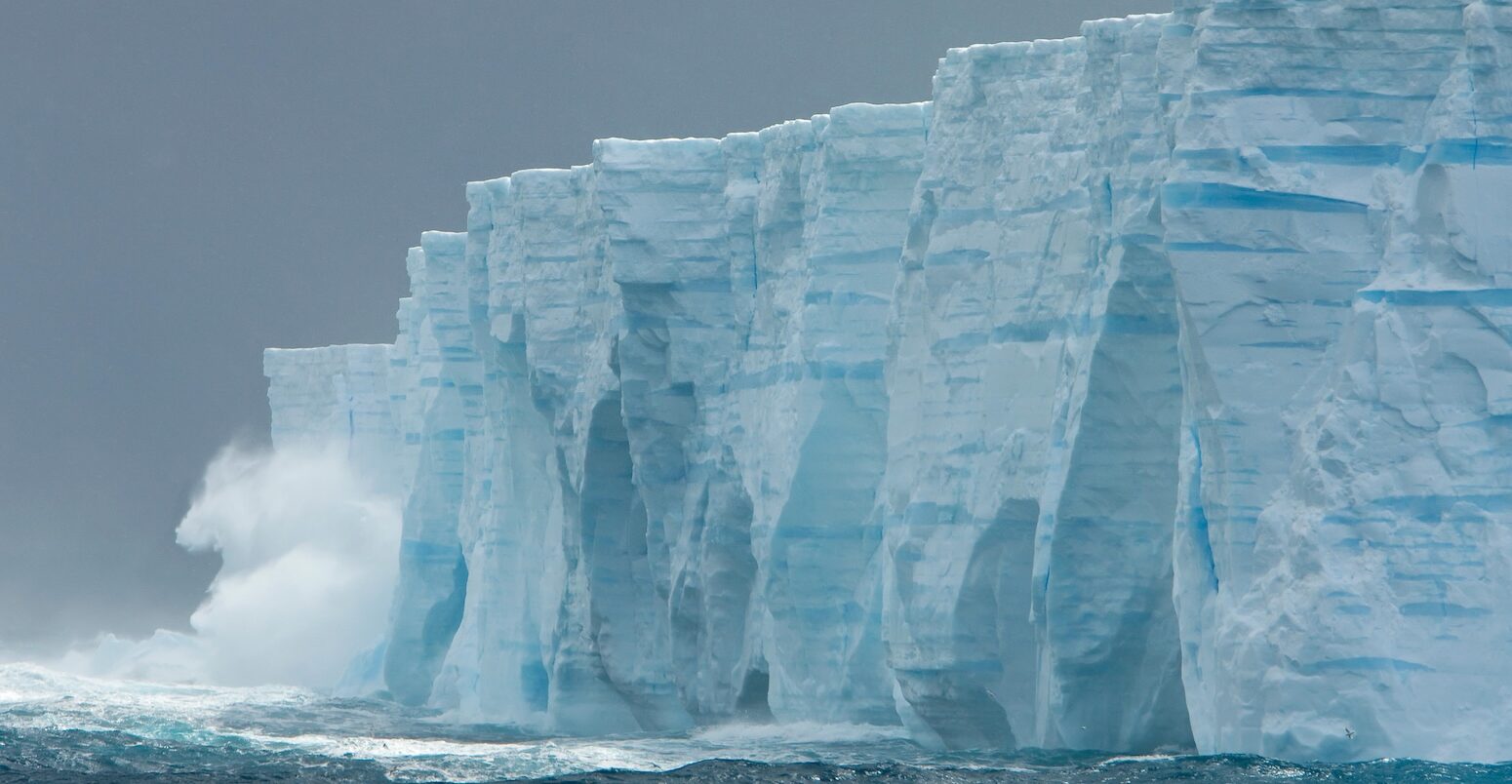 Waves crashing against ice cliffs of iceberg in Southern Ocean.